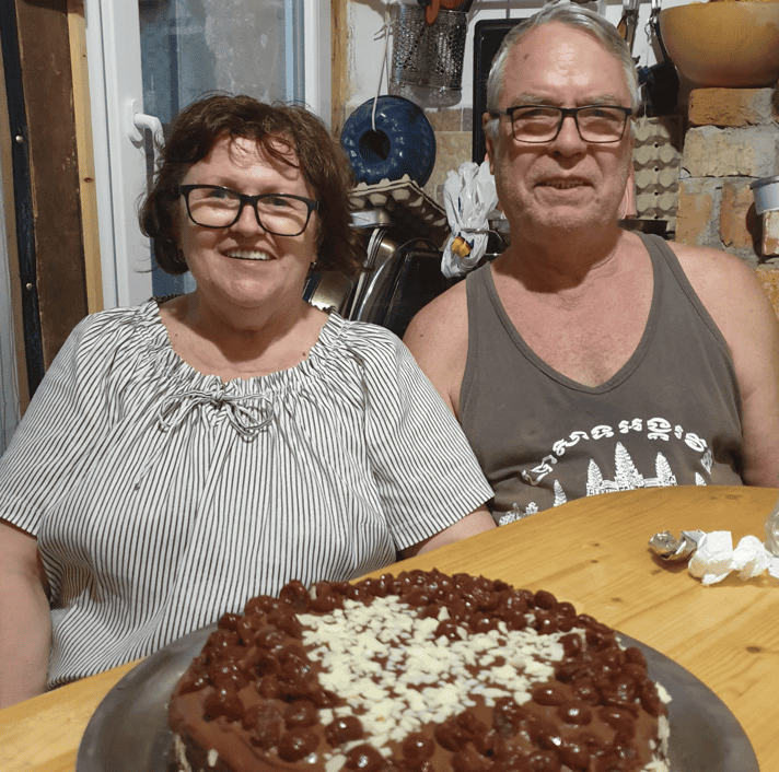 Rebeca Duriga's parents, sitting at a table with a cake on it.