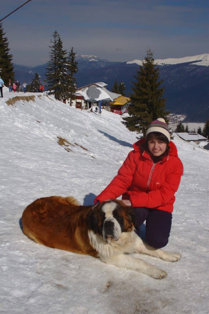 Rebeca Duriga wearing a red jacket and patting a dog in Transylvania.