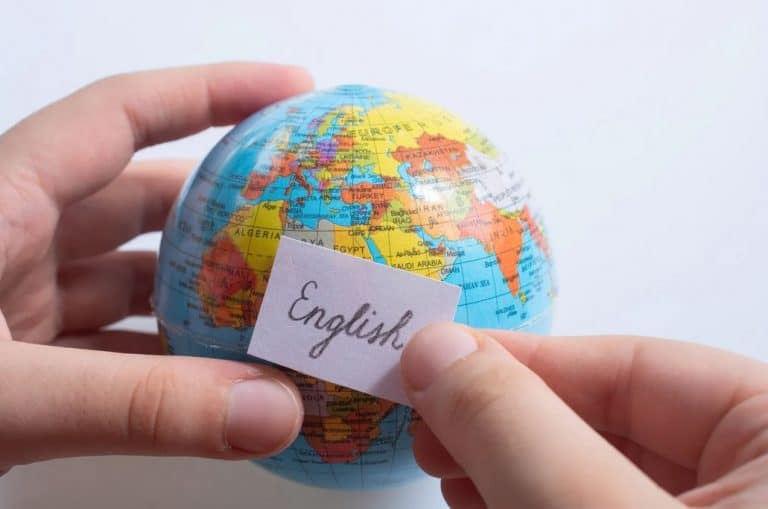 A small globe held by a person who puts a post-it note with the word "English" on it.