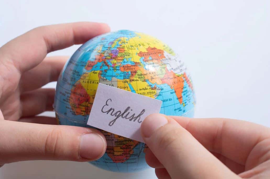 A small globe held by a person who puts a post-it note with the word "English" on it.