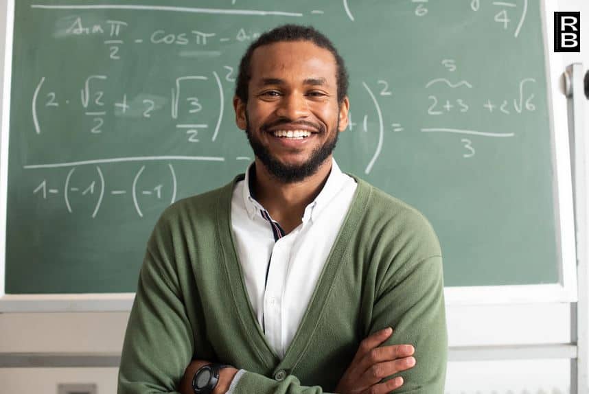 A teacher smiling in front of a board.